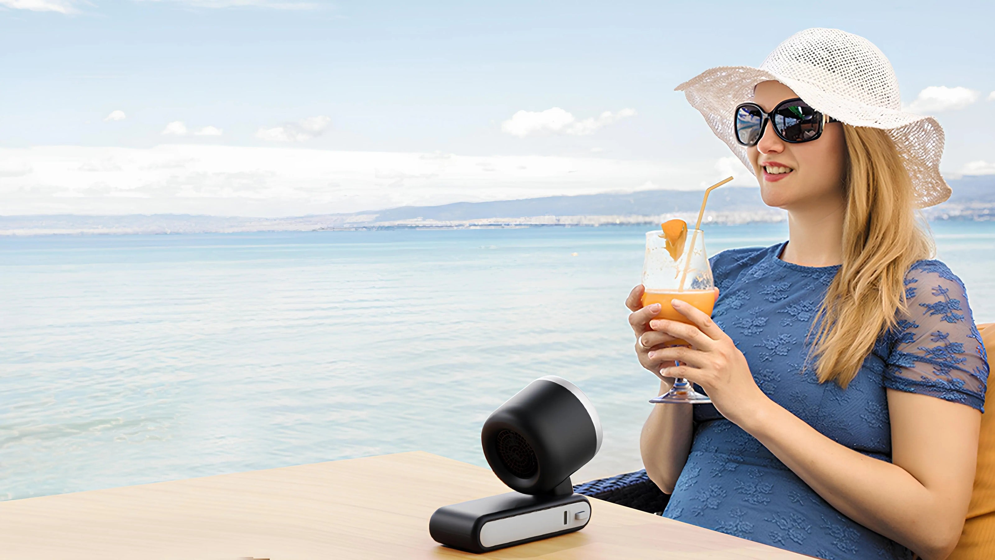 Woman enjoying a refreshing drink on the beach while using a portable fan for comfort